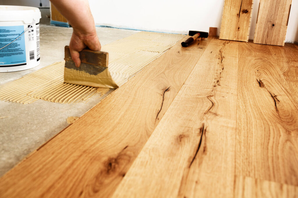man applying glue to install hardwood flooring