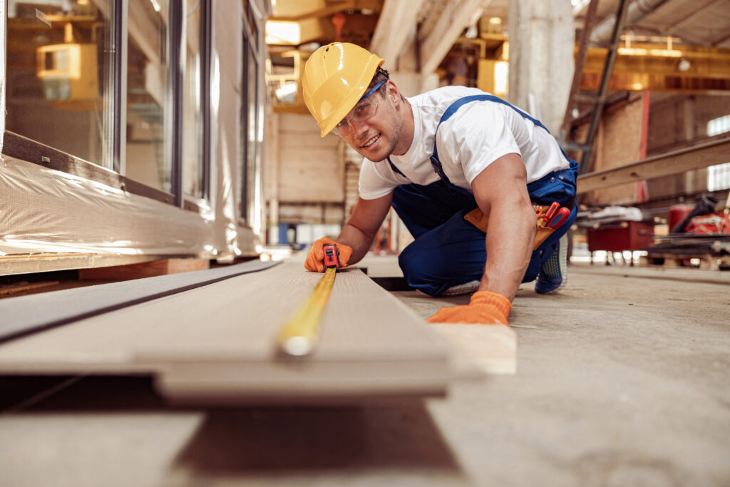 Joyful male builder measuring timber plank at construction site Man measuring wood